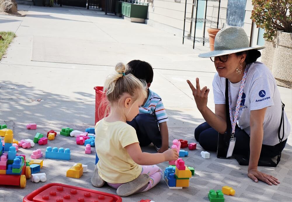 Woman sitting on ground outside with small children playing with Legos